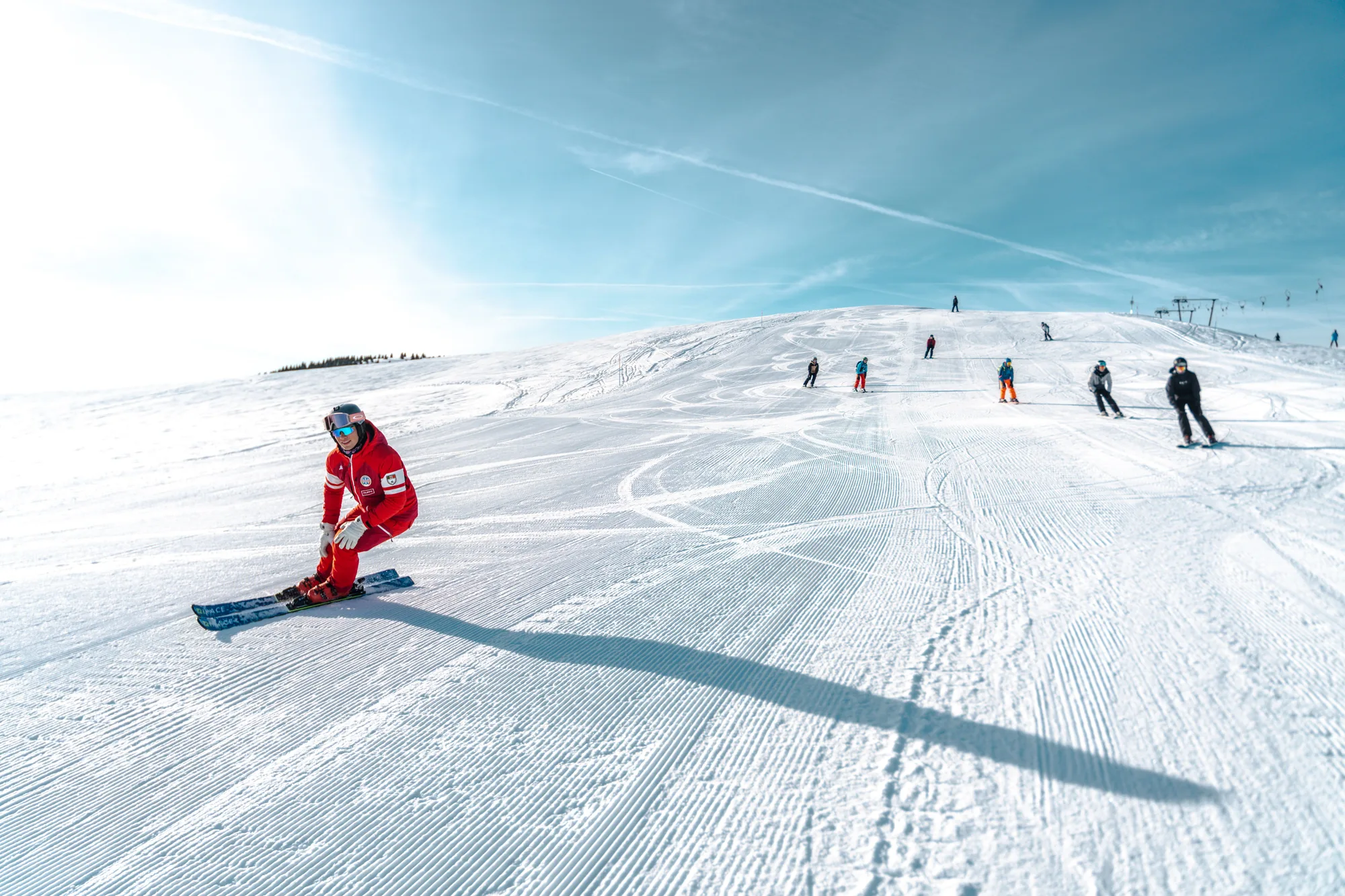 Skieurs sur une piste damée en haute montagne sous le soleil